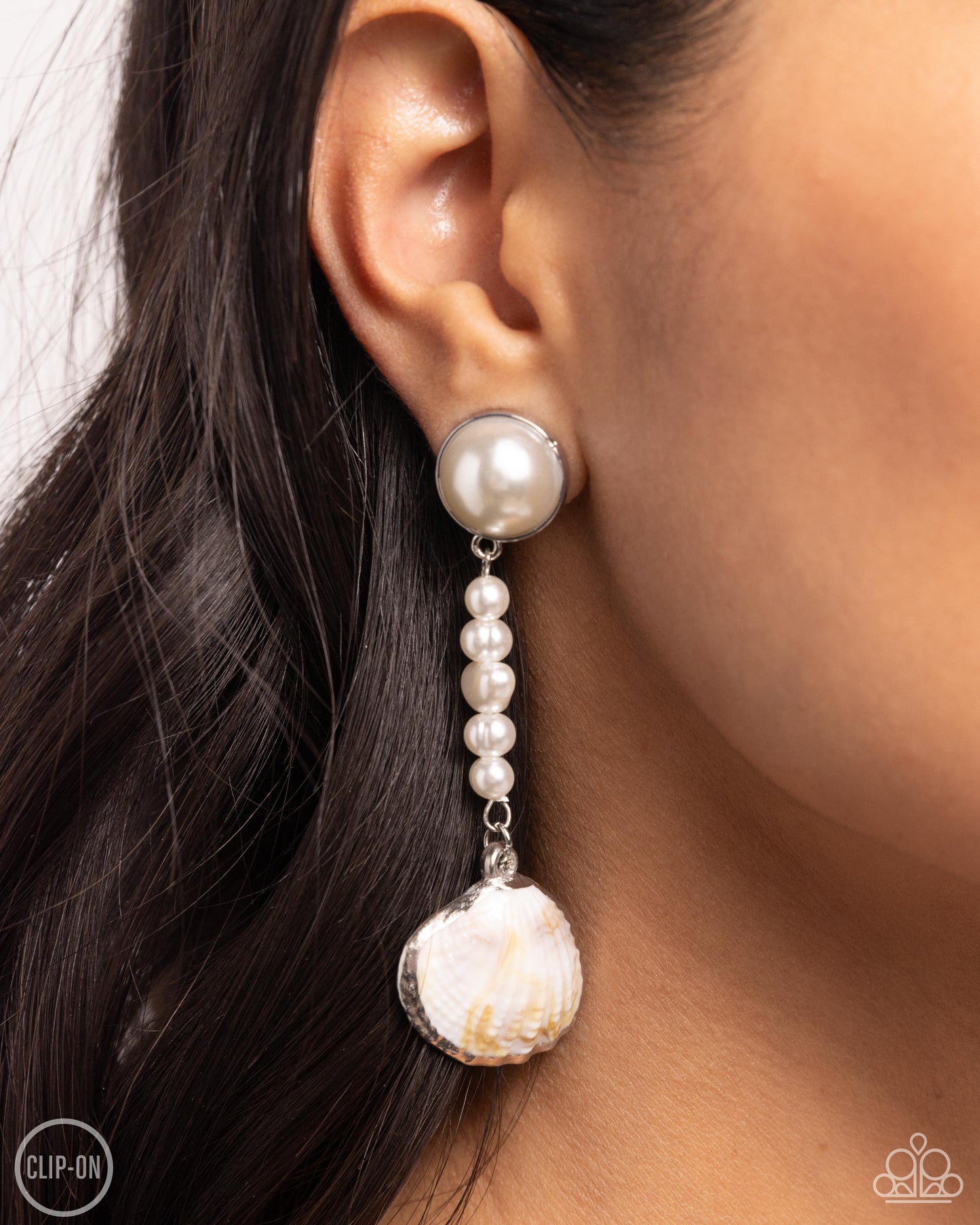 Oceanic Occasion White Seashell Clip-On Earring - Paparazzi Accessories Pressed in a silver fitting, an oversized white pearl gives way to a lengthened strand of glossy classic and baroque white pearls. Bordered in a shimmery silver finish, a white seashell swings from the bottom of the pearly strand for a classy, coastal statement. Earring attaches to a standard clip-on fitting. Sold as one pair of clip-on earrings. SKU: P5CO-WTXX-144XX