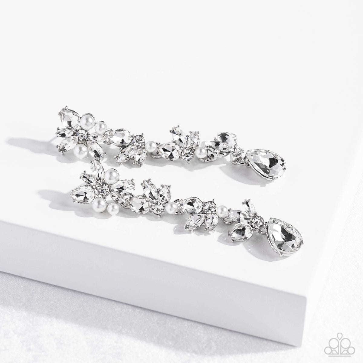 LIGHT at the Opera White Post Earring - Paparazzi Accessories Radiant clusters of white reflective teardrop, marquise-cut and round gems combine with classic white pearls to create an explosion of glitz that extends down the ear. Hanging from the bottom of the light-reflecting earring, a white, reflective teardrop gem swings for some eye-catching shimmer against a backdrop of high-sheen silver. Earring attaches to a standard post fitting. Sold as one pair of post earrings. P5PO-WTXX-360XX