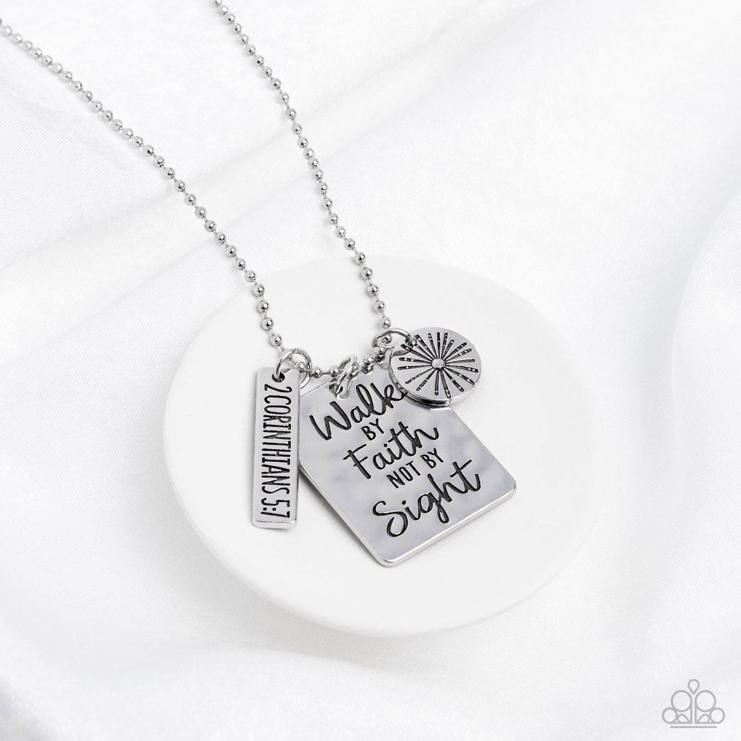 Sunshine Sight Silver Necklace - Paparazzi Accessories Hanging from a silver ball chain, a hammered collection of a rectangular plate dangles next to a disc featuring a sun, and a bar stamped with the Bible reference "2 Corinthians 5:7". The three dangling silver shapes add eye-catching movement to the inspired design. Prominently stamped on the rectangular pendant, the words "Walk by Faith not by Sight" stand out for a faith-filled finish. Features an adjustable clasp closure.