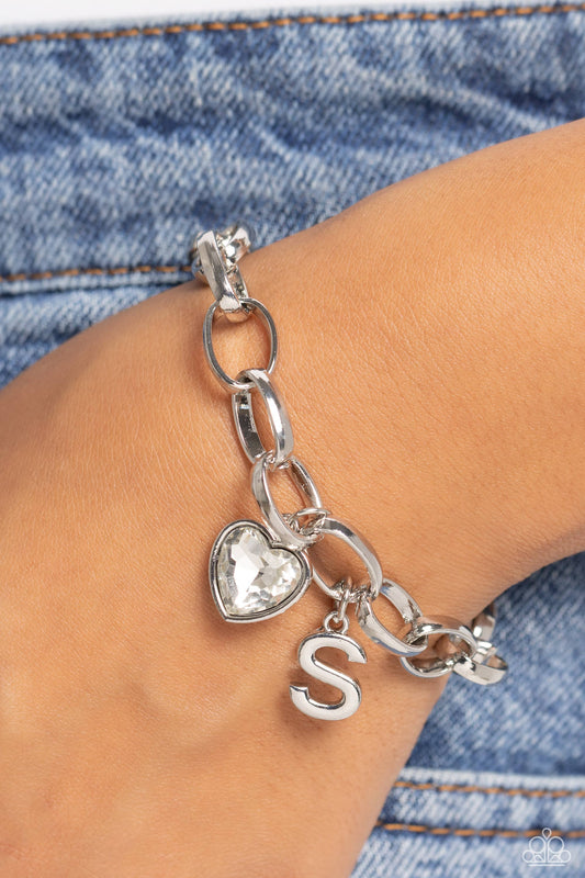 Guess Now Its INITIAL White "S" Bracelet - Paparazzi Accessories  A simple collection of silver charms — including a white rhinestone heart pressed in a silver frame and a sleek letter "S" — dance from a chunky silver chain around the wrist, creating a sentimental fringe. Features an adjustable clasp closure.  Sold as one individual bracelet.  New Kit Sku:  P9BA-WTXX-053XX