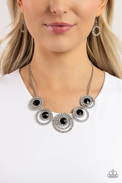 Dramatic Darling Black Necklace - Paparazzi Accessories  Encrusted in glassy white rhinestones, layered silver frames delicately connect below the collar for a statement-making finish. Featured in the center of the effervescent rings, faceted black beads come to a point for a dramatic touch of color along the neckline. Features an adjustable clasp closure.  Sold as one individual necklace. Includes one pair of matching earrings.  SKU: P2RE-BKXX-470XX
