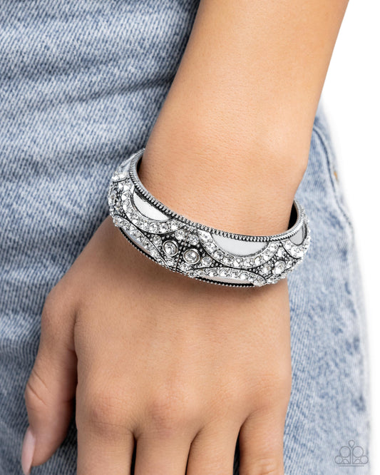 Draped in Decadence White Rhinestone Hinge Bracelet - Paparazzi Accessories  Featuring a dazzling array of white rhinestones and silver studs, a refined pattern curls up and along a high-sheen silver cuff. Features a hinged closure.  Sold as one individual bracelet.  SKU: P9ST-WTXX-060XX