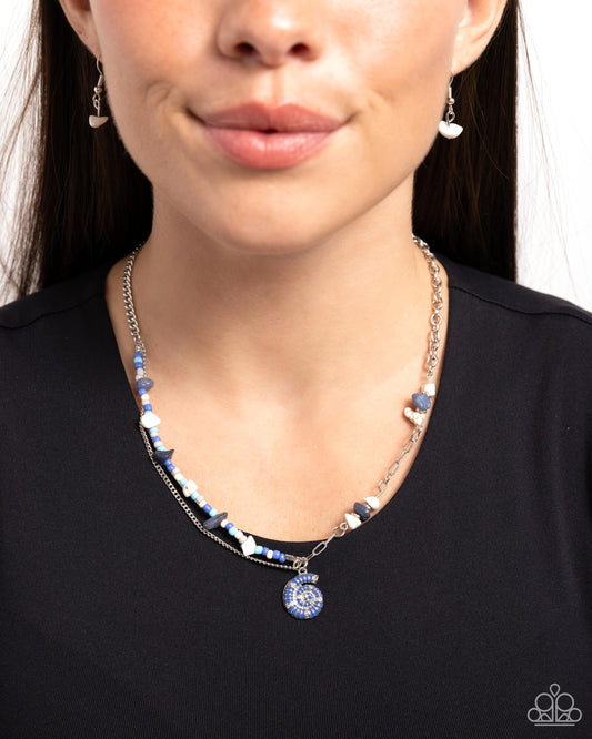 Spiraling Seafloor Blue Necklace - Paparazzi Accessories Infused along an abstract silver chain, a collection of silver studs, lapis, and white stones, and ivory, gray, light blue, and marlin seed beads coalesce below the neckline. A Marlin-painted silver spiral seashell cascades from the display for a charming, coastal finish. Features an adjustable clasp closure. As the stone elements in this piece are natural, some color variation is normal. SKU: P2SE-BLXX-562XX