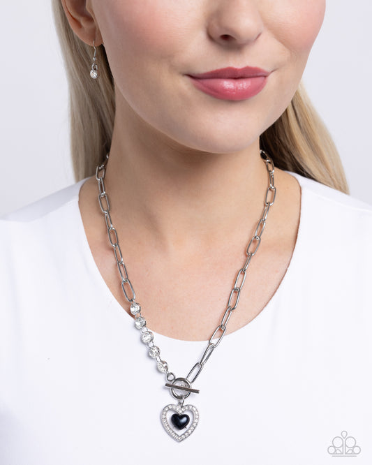 Soft-Hearted Style Black Heart Necklace - Paparazzi Accessories A gleaming black acrylic heart is nestled inside an airy, white rhinestone-encrusted heart frame, creating a charming pendant at the bottom of an exaggerated silver paperclip chain. A quintet of white gems interrupts the silver paperclip chain for additional refinement and shimmer. Features a toggle clasp closure. Sold as one individual necklace. Includes one pair of matching earrings. SKU: P2RE-BKXX-483XX