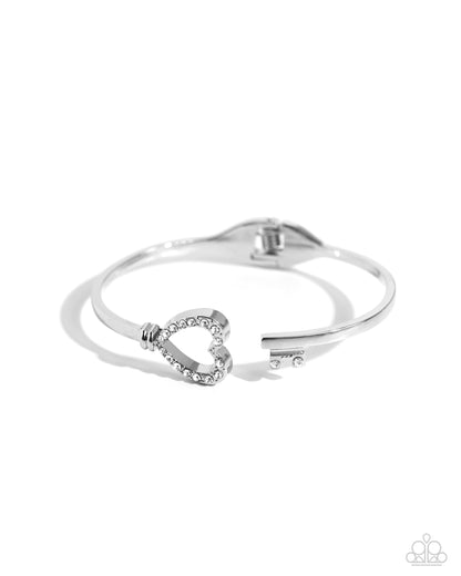 The Key to Romance White Hinge Bracelet - Paparazzi Accessories  Embellished in white rhinestones, a silver heart frame is seemingly unlocked by a white rhinestone-encrusted key that spans across the other side of the wrist for a padlock-inspired centerpiece. Features a hinged closure.  Sold as one individual bracelet.  SKU: P9RE-WTXX-605XX