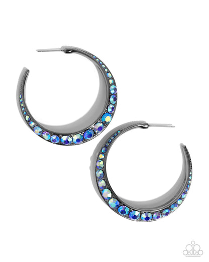 Embedded Edge Blue Hoop Earring - Paparazzi Accessories  The front-facing surface of a chunky gunmetal hoop is dipped in layers of brilliantly sparkling sapphire iridescent rhinestones that gradually increase in size towards the center of the hoop while light-catching gunmetal studs frame the ends for a blinding finish. Earring attaches to a standard post fitting. Hoop measures 1 3/4" in diameter. Due to its prismatic palette, color may vary.  Sold as one pair of hoop earrings.  P5HO-BLXX-055XX