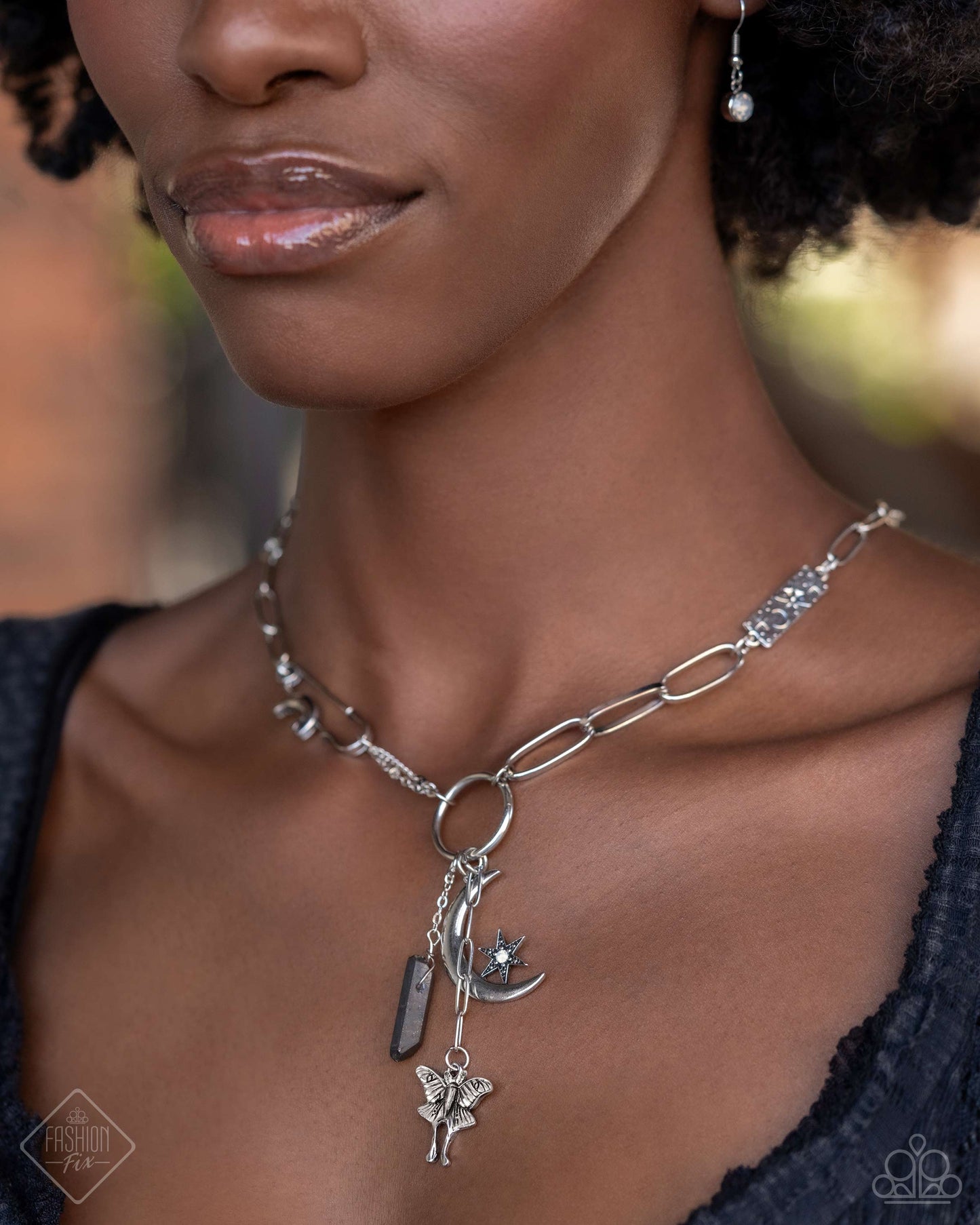 Celestial Confidence - Silver Item #P2WH-SVXX-387YC A dainty silver paperclip chain gradually increases in size as it elongates down the neckline, accentuated by a link resembling a safety pin, dotted with a crescent moon, and embossed with starry details. The embellished chain leads to a collection of charms, including a chiseled piece of hematite, a three-dimensional star nestled in the curve of a crescent moon, and a moth with intricate detailing. Includes one pair of matching earrings.