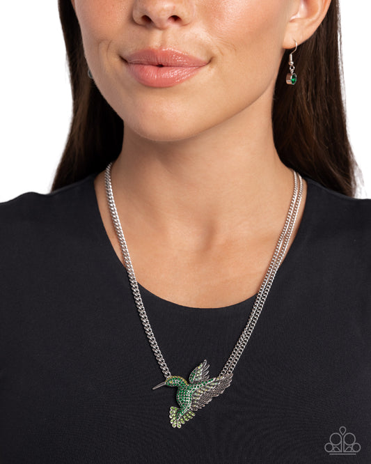 Hummingbird Headline Green Necklace - Paparazzi Accessories  Embellished in green multicolored and green iridescent rhinestones, a textured silver hummingbird pendant flutters below the neckline from a silver chain attached to its head and a double-layered silver chain attached to its wings for a whimsically supported look. Features an adjustable clasp closure. Due to its prismatic palette, color may vary.  Sold as one individual necklace. Includes one pair of matching earrings.  P2WH-GRXX-417XX