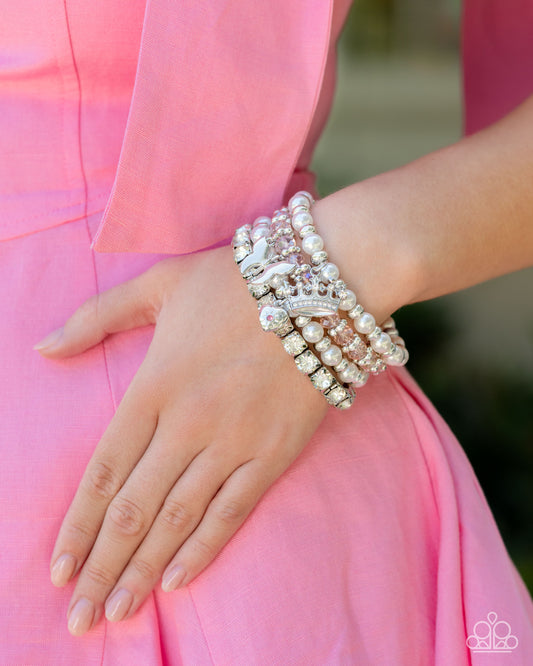 Feminine Charm Pink Charm Stretch Bracelet - Paparazzi Accessories  Infused along elastic stretchy bands, a glistening stack of four bracelets featuring silver wheel beads, silver discs, white pearls, white rhinestones in thick silver square fittings, and faceted glassy pink beads with a subtle UV shimmer are adorned with a silver butterfly, white rhinestone-encrusted crown, and rose rhinestone-centered floral heart, creating soft, charming layers around the wrist.  Sold as one set of four bracelets.  P9ST-