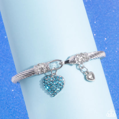 Heart Hour Blue Hook and Eye Bracelet - Paparazzi Accessories  Rippling with wavy textures, a glistening band of silver coils and twists along the wrist for a timeless display. An aquamarine rhinestone-encrusted silver heart swings from one end of the display while a dainty, solitaire silver heart swings from the other for a beautifully balanced look. Textured silver and rows of white rhinestones adorn the closures for additional refinement and glitz. Features a hook and eye closure.  Sold as one individual
