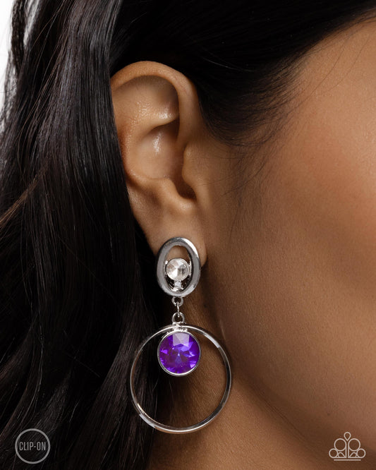 Modern Moment Purple Clip-On Earring - Paparazzi Accessories  Pressed in a silver frame, a faceted white gem glistens in the center of an airy silver oval, giving way to a faceted flashy amethyst gem suspended along the center of a dainty silver hoop, creating a playful pop of color. Earring attaches to a standard clip-on fitting.  Sold as one pair of clip-on earrings.  P5CO-PRXX-028XX