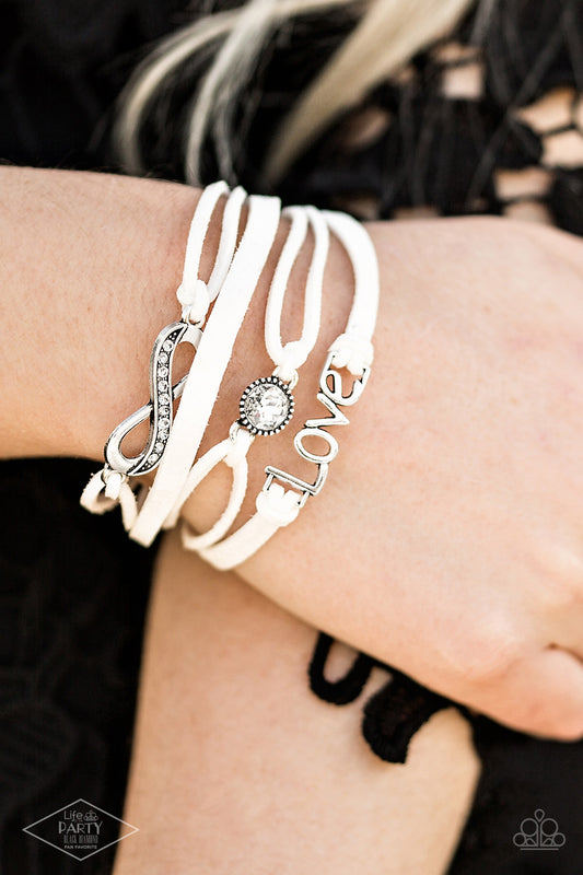 Infinitely Irresistible White Bracelet - Paparazzi Accessories  Strands of white suede knot around silver charms, including a glittery infinity charm, a solitaire rhinestone, and a charm whimsically spelling out “love” across the wrist. Features an adjustable clasp closure.  Sold as one individual bracelet. This Fan Favorite is back in the spotlight at the request of our 2021 Life of the Party member with Black Diamond Access, Miranda B.