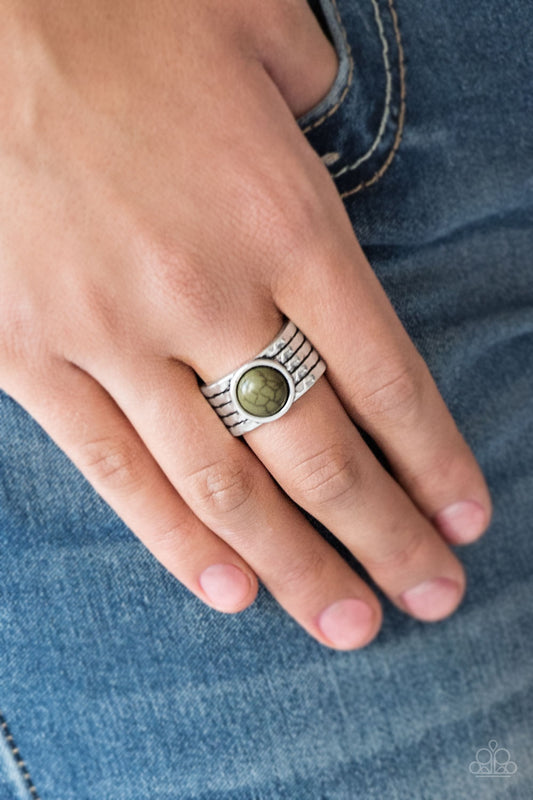Blooming Badlands Green Ring - Paparazzi Accessories  Antiqued lines race across a thick silver band, creating the illusion of stacked bands. An earthy green stone is pressed into the center of the delicately hammered band for a seasonal finish. Features a stretchy band for a flexible fit.  Sold as one individual ring.