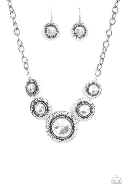 Global Glamour White Necklace - Paparazzi Accessories.  Gradually increasing in size, dramatically oversized white gems are pressed into the centers of hammered and silver studded frames. The blinding frames link below the collar for a glamorous, statement-making finish. Features an adjustable clasp closure.  ﻿All Paparazzi Accessories are lead free and nickel free!  Sold as one individual necklace. Includes one pair of matching earrings.