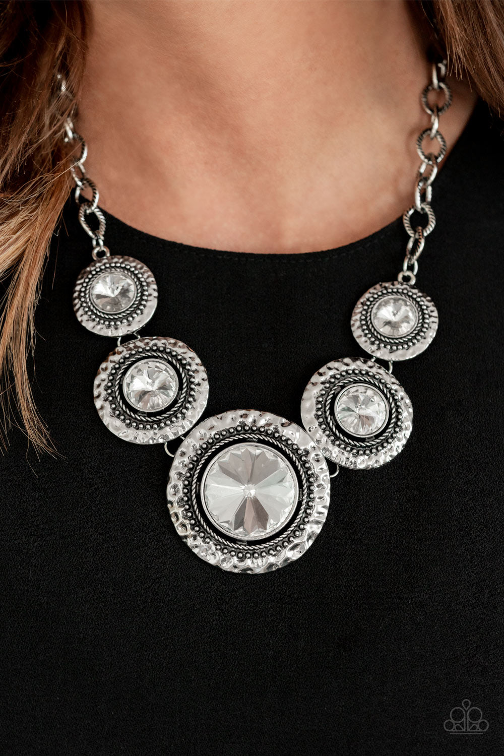 Global Glamour White Necklace - Paparazzi Accessories.  Gradually increasing in size, dramatically oversized white gems are pressed into the centers of hammered and silver studded frames. The blinding frames link below the collar for a glamorous, statement-making finish. Features an adjustable clasp closure.  ﻿All Paparazzi Accessories are lead free and nickel free!  Sold as one individual necklace. Includes one pair of matching earrings.