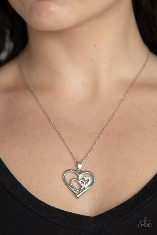 Cupid Charm White Necklace - Paparazzi Accessories  A white rhinestone encrusted heart intertwines with a plain silver heart inside of a larger silver heart frame, creating a romantic pendant at the bottom of a shimmery silver chain. Features an adjustable clasp closure.  All Paparazzi Accessories are lead free and nickel free!   Sold as one individual necklace. Includes one pair of matching earrings.