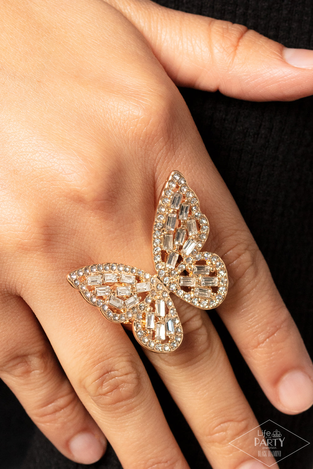 Flauntable Flutter Gold Butterfly Ring - Paparazzi Accessories Item #P4RE-GDXX-218XX Dainty white emerald cut rhinestones are sprinkled across the golden wings of a butterfly that is encrusted in glassy white rhinestones for a dramatically dazzling finish. Features a stretchy band for a flexible fit.  Sold as one individual ring. This Black Diamond Encore is back in the spotlight at the request of our 2022 Life of the Party member with Black Diamond Access, Karla N.