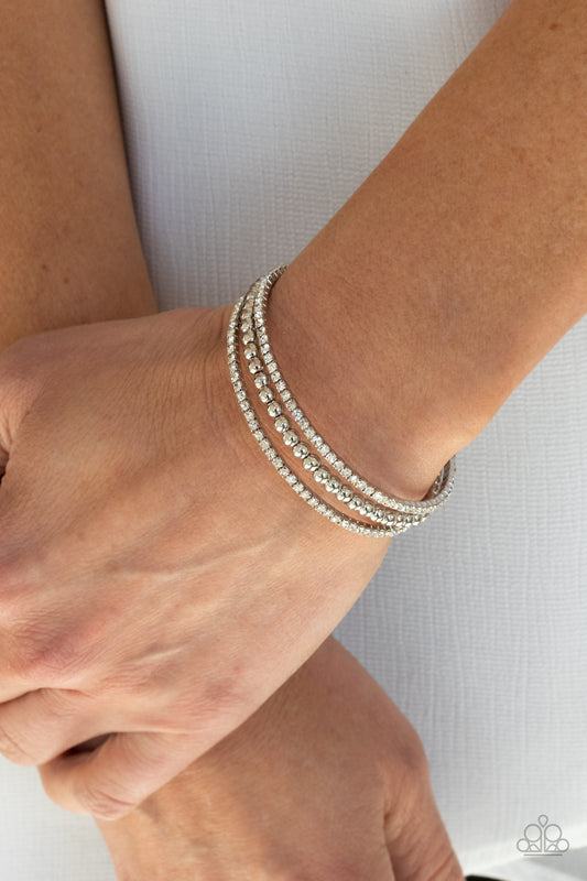 High-End Eye Candy White Cuff Bracelet - Paparazzi Accessories. Two strands of dazzling white rhinestones flank a row of shiny silver beads, coalescing into a sparkly layered cuff around the wrist.  All Paparazzi Accessories are lead free and nickel free!  Sold as one individual bracelet.