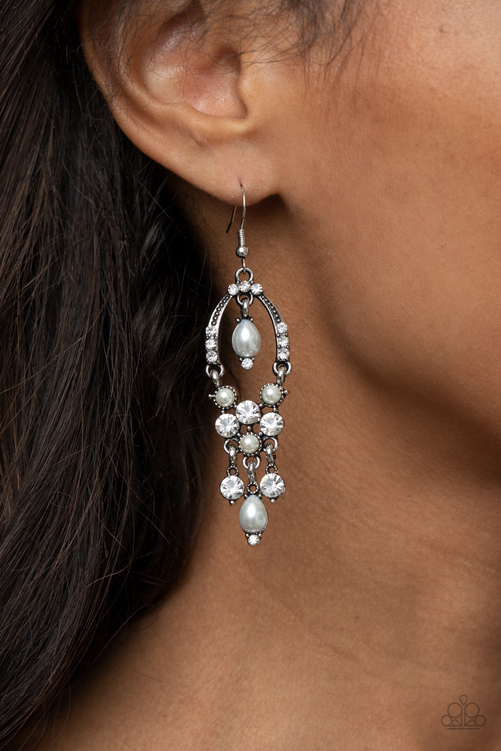 Back In The Spotlight White Earring - Paparazzi Accessories. Glittery white rhinestones and pearly white beaded fittings delicately swing from the bottom of an ornately embellished oval frame. A matching pearly frame dangles from the top of the decorative silver frame, adding a timeless movement to the sparkly display. Earring attaches to a standard fishhook fitting.  All Paparazzi Accessories are lead free and nickel free!  Sold as one pair of earrings.