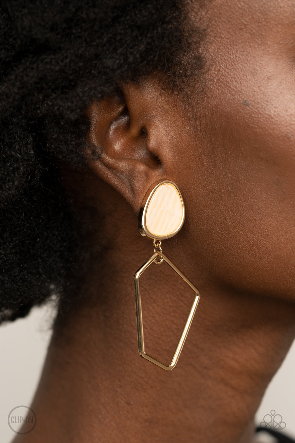 Retro Reverie Gold Clip-On Earring - Paparazzi Accessories  Encased in a classic gold fitting, an abstract faux stone fitting gives way to an airy geometric gold frame for a refined asymmetrical look. Earring attaches to a standard clip-on fitting.  All Paparazzi Accessories are lead free and nickel free!  Sold as one pair of clip-on earrings.