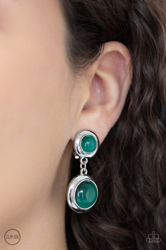 Subtle Smolder Green Clip-On Earring - Paparazzi Accessories  Encased in sleek silver fittings, two green cat's eye stones link into a whimsical lure. Earring attaches to a standard clip-on fitting.  All Paparazzi Accessories are lead free and nickel free!  Sold as one pair of clip-on earrings.