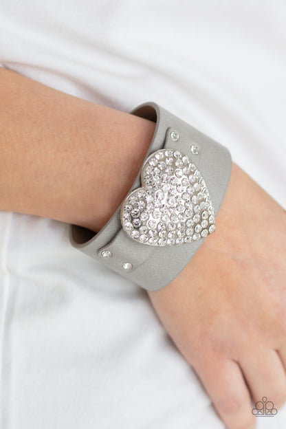 Flauntable Flirt Silver Wrap Bracelet - Paparazzi Accessories  Encrusted in blinding white rhinestones, an oversized silver heart frame is studded in place across the front of a gray leather band, creating a flirtatious centerpiece around the wrist. Features an adjustable snap closure.  All Paparazzi Accessories are lead free and nickel free!  Sold as one individual bracelet.