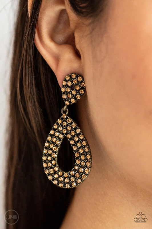 Pack In The Pizzazz Brass Clip-On Earring - Paparazzi Accessories  A topaz rhinestone encrusted silhouette teardrop attaches to the bottom of a dainty topaz rhinestone encrusted teardrop, creating a glamorous lure. Earring attaches to a standard clip-on fitting.  All Paparazzi Accessories are lead free and nickel free!  Sold as one pair of clip-on earrings.