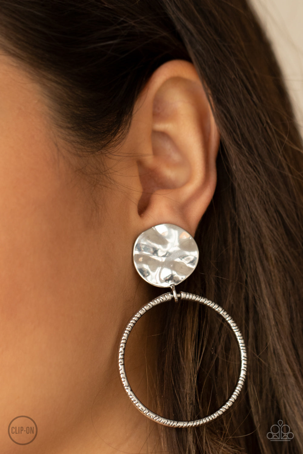 Undeniably Urban Silver Clip-On Earring - Paparazzi Accessories  A textured silver hoop attaches to a hammered silver disc, creating an edgy hoop. Earring attaches to a standard clip-on fitting.  All Paparazzi Accessories are lead free and nickel free!  Sold as one pair of clip-on earrings.