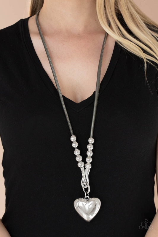 Forbidden Love Silver Necklace - Paparazzi Accessories  Featuring chunky silver beads, an oversized silver heart pendant swings from dramatic silver hook-like fittings that attach to a bold gray leather cord draped across the chest for a haute heartbreaker look. Features an adjustable clasp closure.  All Paparazzi Accessories are lead free and nickel free!  Sold as one individual necklace. Includes one pair of matching earrings.