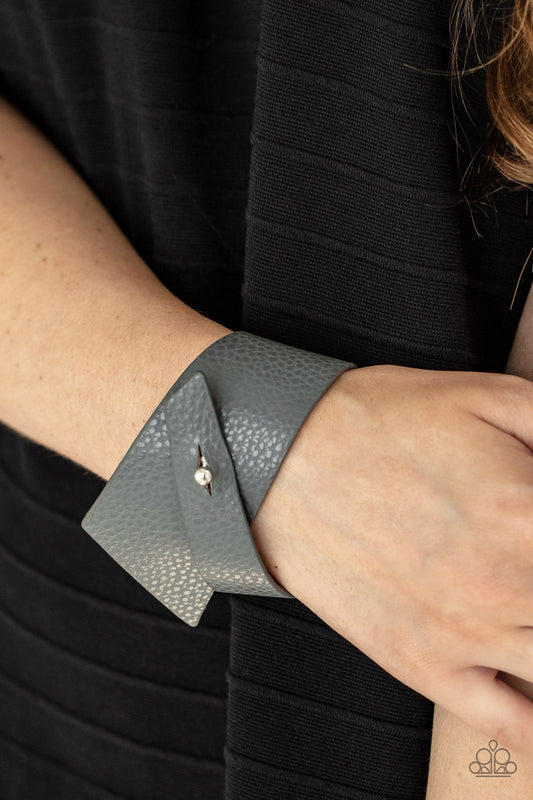 PIECE Offering Silver Bracelet - Paparazzi Accessories.  A triangular piece of Ultimate Gray leather delicately wraps around the wrist, creating an edgy asymmetrical centerpiece around the wrist. Features a studded button loop closure.  ﻿﻿﻿All Paparazzi Accessories are lead free and nickel free!  Sold as one individual bracelet.