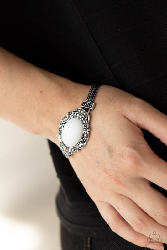 Top-Notch Drama White Bracelet - Paparazzi Accessories  Hematite encrusted silver frames delicately overlap around an oval white bead, creating an edgy centerpiece. The colorful centerpiece attaches to strands of ornate silver chains that are held in place around the wrist by studded silver frames. Features an adjustable clasp closure.  ﻿All Paparazzi Accessories are lead free and nickel free!  Sold as one individual bracelet.