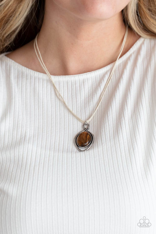 Desert Mystery Brown Necklace - Paparazzi Accessories  An oversized tiger's eye stone is pressed into a silver oval frame and outlined with an unexpected irregular shaped frame. The eye-catching pendant suspends from a double strand of white cord below the collar for a mysterious finish. Features an adjustable clasp closure.  All Paparazzi Accessories are lead free and nickel free!   Sold as one individual necklace.