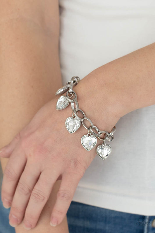 Candy Heart Charmer White Bracelet - Paparazzi Accessories  White heart-shaped gems are encased in sleek silver frames that swing from an oversized silver chain, creating a sparkly fringe around the wrist. Features an adjustable clasp closure.  All Paparazzi Accessories are lead free and nickel free!   Sold as one individual bracelet.