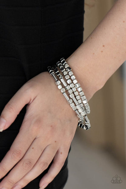 Metro Materials Silver Bracelet - Paparazzi Accessories. Lightweight and flirty, two strands of silver square beads interspersed with silver cylinders, are paired with two strands of silver cubes. The four stretchy bracelets come together to create an irresistible stack of metallic mayhem.  All Paparazzi Accessories are lead free and nickel free!  Sold as one set of four bracelets.