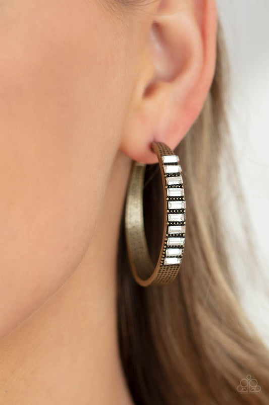 More To Love Brass Hoop Earring - Paparazzi Accessories  The top half of a thick textured brass frame is lined in a stack of emerald cut white rhinestones, creating an unexpected pop of shimmer. Earring attaches to a standard post fitting. Hoop measures approximately 1 3/4” in diameter.  All Paparazzi Accessories are lead free and nickel free!  Sold as one pair of hoop earrings.