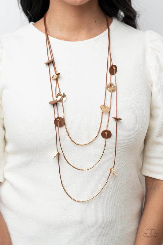 Alluring Luxe - Brown Item #P2SE-BNXX-193XX Shining wavy gold discs and brown leather discs adorn a trio of lengthened subtly shimmering brown cords. Rows of dainty gold cylinders are threaded along the bottom of each cord adding luxurious allure to the piece. Features an adjustable clasp closure.  Sold as one individual necklace. Includes one pair of matching earrings.