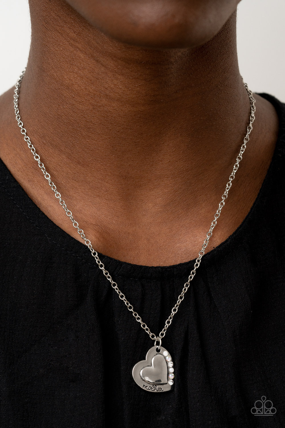 Happily Heartwarming White Necklace - Paparazzi Accessories  Stamped in the word, "Mother," an embossed heart pendant is encrusted in a row of white and iridescent rhinestones, creating a sparkly sentimental centerpiece below the collar. Features an adjustable clasp closure.  Sold as one individual necklace. Includes one pair of matching earrings.