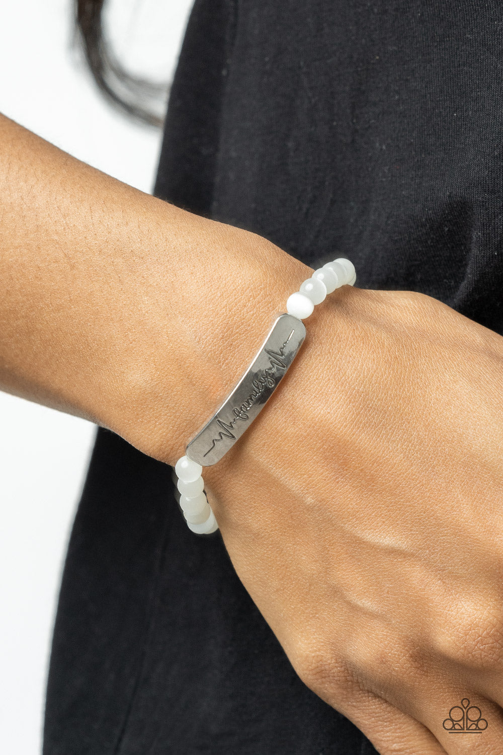 Family is Forever White Bracelet - Paparazzi Accessories  Stamped in heartbeats and the word, "Family," a shiny silver plate attaches to a strand of white cat's eye stone beads that are threaded along a stretchy band, creating a whimsically sentimental centerpiece around the wrist.  Sold as one individual bracelet.
