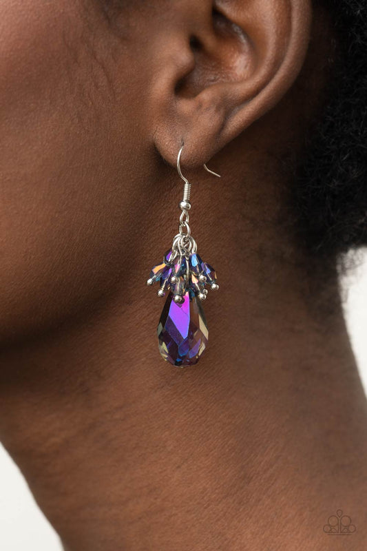 Well Versed in Sparkle Purple Earring - Paparazzi Accessories  A cluster of dainty oil spill iridescent beads delicately overlap atop an oversized smoky purple iridescent teardrop gem, creating a sparkly chandelier. Earring attaches to a standard fishhook fitting.  All Paparazzi Accessories are lead free and nickel free!  Sold as one pair of earrings.