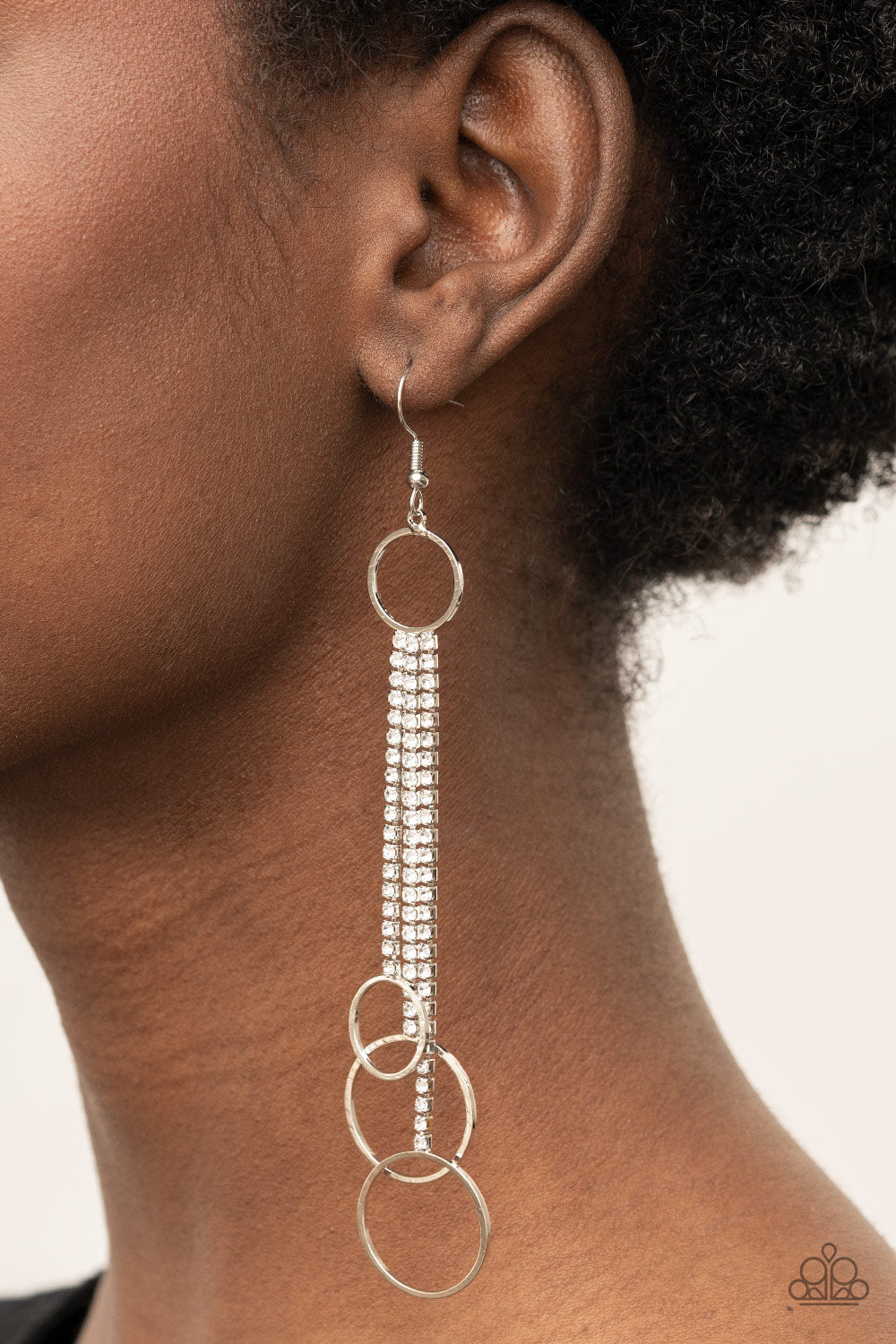 Demurely Dazzling White Earring - Paparazzi Accessories  Dainty silver hoops swing from the bottom of glittery strands of glassy white rhinestones that attach to the bottom of a dainty silver ring, creating a tantalizing tassel. Earring attaches to a standard fishhook fitting.  All Paparazzi Accessories are lead free and nickel free!  Sold as one pair of earrings.