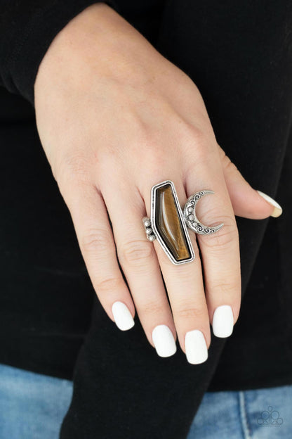 Cosmic Karma Brown Ring - Paparazzi Accessories  Encased in a raised silver fitting, a geometric tiger's eye stone is flank by a decorative row of silver studs and an ornate half moon frame for a seasonal statement. The oversized frame is attentional, creating the illusion of multiple rings. Features a stretchy band for a flexible fit.  All Paparazzi Accessories are lead free and nickel free!  Sold as one individual ring.
