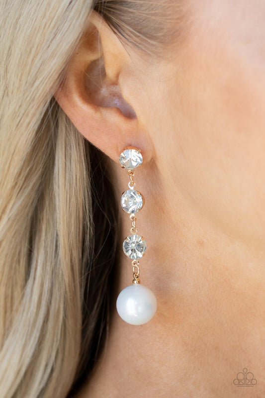 Yacht Scene Gold Earring - Paparazzi Accessories  Encased in sleek gold fittings, a trio of classic white rhinestones give way to an oversized iridescent pearl, creating an elegantly extended chandelier. Earring attaches to a standard post fitting.  Sold as one pair of post earrings.