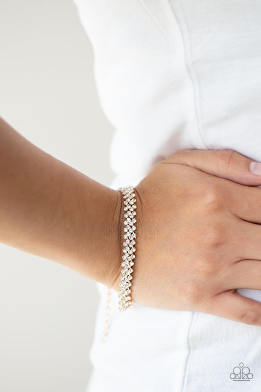 Chicly Candescent Gold Bracelet - Paparazzi Accessories  Featuring sleek gold fittings, dainty rows of glassy white rhinestones delicately slant across the wrist, coalescing into a timeless centerpiece. Features an adjustable clasp closure.  All Paparazzi Accessories are lead free and nickel free!  Sold as one individual bracelet.