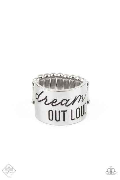 Dream Louder Silver Ring - Paparazzi Accessories  The front of a thick silver band is stamped in the phrase, "Dream out loud," creating an inspirational centerpiece across the finger. Features a stretchy band for a flexible fit.  All Paparazzi Accessories are lead free and nickel free!  Sold as one individual ring.