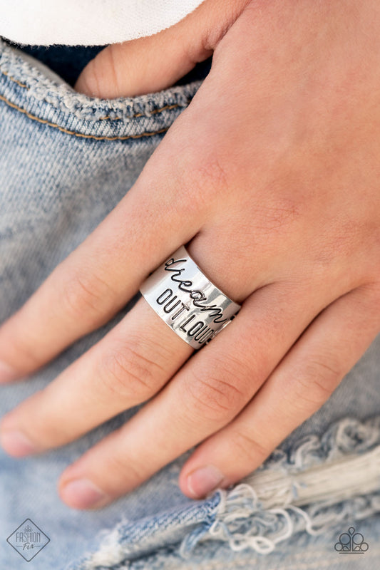 Dream Louder Silver Ring - Paparazzi Accessories  The front of a thick silver band is stamped in the phrase, "Dream out loud," creating an inspirational centerpiece across the finger. Features a stretchy band for a flexible fit.  All Paparazzi Accessories are lead free and nickel free!  Sold as one individual ring.