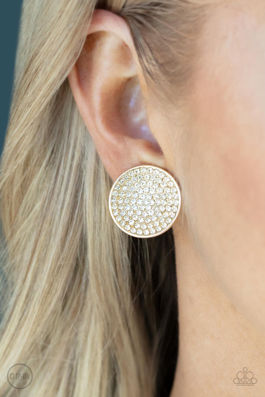 Drama on Demand Gold Clip-On Earring - Paparazzi Accessories  Sparkling with brilliance, a concave shiny gold disc encompasses radiating rows of shimmering white rhinestones creating a striking impact. Earring attaches to a standard clip-on fitting.  Sold as one pair of clip-on earrings.