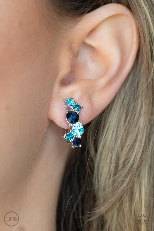 Cosmic Celebration Blue Clip-On Earring - Paparazzi Accessories  Varying in shades of blue, mismatched rhinestones delicately coalesce into a dainty frame for a colorfully sparkly display. Earring attaches to a standard clip-on fitting.  Sold as one pair of clip-on earrings.