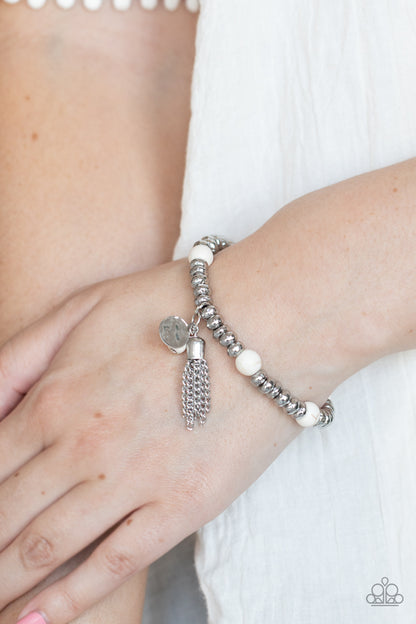 Whimsically Wanderlust White Bracelet - Paparazzi Accessories. An earthy collection of hammered silver beads and round white stones are threaded along a stretchy band around the wrist. A dainty silver tassel, hammered silver disc, and a white stone swing from the seasonal display, adding playful movement to the whimsy look.  All Paparazzi Accessories are lead free and nickel free!  Sold as one individual bracelet.