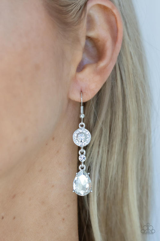Graceful Glimmer White Earring - Paparazzi Accessories  A silver frame dotted in glassy white rhinestones, a solitaire white rhinestone, and an oversized white teardrop gem delicately link into a graceful lure. Earring attaches to a standard fishhook fitting.  All Paparazzi Accessories are lead free and nickel free!   Sold as one pair of earrings.