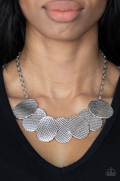 Industrial Wave Silver Necklace - Paparazzi Accessories Item #P2ST-SVXX-170XX A row of gently warped silver discs link together in an overlapping fashion as they connect on each end to a silver chain. Etched in a hammered antiqued silver finish, the oval discs create an edgy industrial effect below the collar. Features an adjustable clasp closure.  Sold as one individual necklace. Includes one pair of matching earrings.